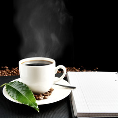 Cup of coffee with haze with notebook and coffee leaf at breakfast