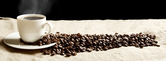Obrazy na Szkle  Panoramiczny widok spienionej filiżanki kawy z ziarnami na tkaninie lnianej