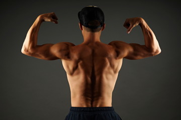 Fototapeta premium Young athlete man shows his muscular back on gray background