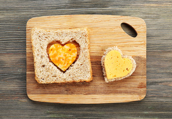 Bread slice with cut in shape of heart and cheese on wooden background