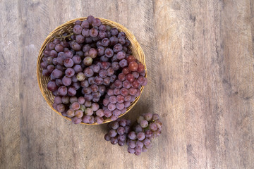 Some red grapes in a wooden pot over a wooden surface seen from
