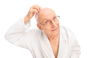Obraz premium Senior man in a white bathrobe checking his hair
