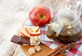Ripe apple, cinnamon and fruit drink in glass teapot on wooden