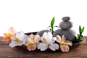Obraz na płótnie Canvas Spa stones with alstroemeria and bamboo in wooden tray with water isolated on white