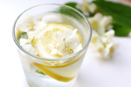Glass of cold refreshing summer drink with flowers and slices of lemon on table close up