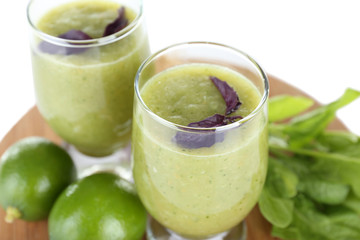 Glasses of green healthy juice with spinach and limes on wooden stand close up