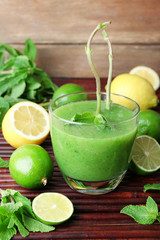 Glass of green healthy juice with mint and fruits on wooden background