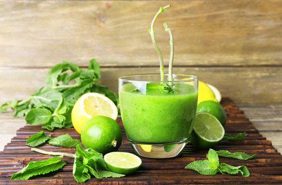 Glass of green healthy juice with mint and fruits on wooden background