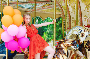 Lifestyle concept, happy young woman with colorful latex balloons in the amusement park riding a carousel