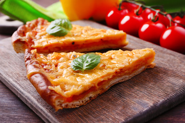 Slices of tasty cheese pizza with basil and vegetables on table close up