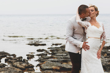 beautiful  gorgeous blonde bride  and stylish groom kissing, on the background of a sea, wedding ceremony  on cyprus.