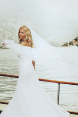 Fototapeta na wymiar dynamic stylish blonde bride posing on the deck of a yacht on the background of sea and mountains Montenegro