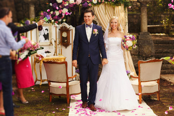 uests throw the petals on confetti on happy married bride and groom after the wedding ceremony