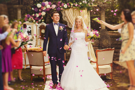 uests throw the petals on confetti on happy married bride and groom after the wedding ceremony