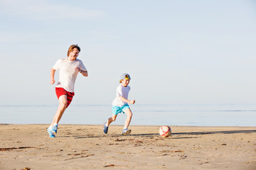 Happy father and son play soccer or football on the beach