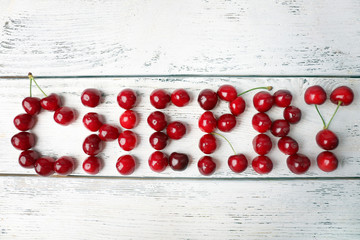 Sweet cherries making word Cherry on wooden background