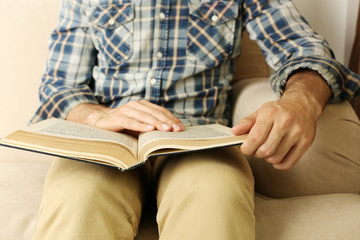 Young man reading book on sofa close up