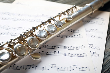 Naklejka premium Silver flute with music notes on wooden table close up
