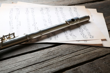 Silver flute with music notes on wooden table close up