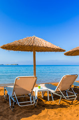 Straw umbrellas and sunbeds on a red sand beach and turquoise water.