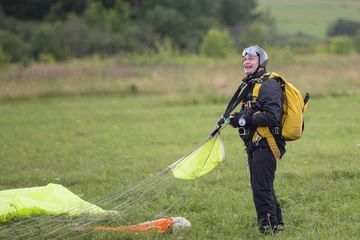 Tuinposter Joyful man in black suit with yellow parachute standing on green field after jump © Aleksei Lazukov