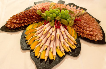 Gemischte Schinkenplatte auf Ahornförmiger Platte mit Weintrauben und Melonen