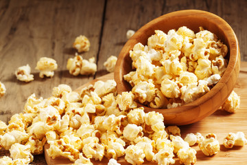 Caramel popcorn poured from a wooden bowl, selective focus