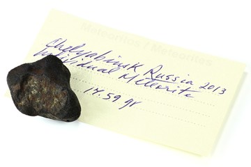 Fragment des Chelyabinsk Meteoriten mit Bestimmungszettel isoliert auf weißem Hintergrund