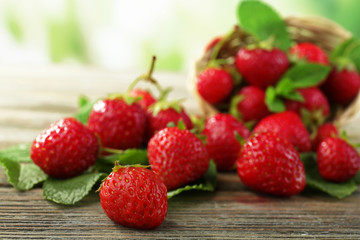 Ripe strawberries with leaves in wicker basket on wooden table on blurred background