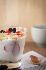 Glass of home made yogurt with cereals, strawberry and banana sliced.