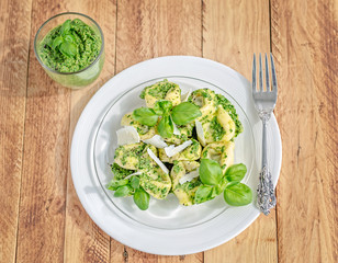Top view of a plate of basil ricotta tortelloni with pesto and parmesan flakes and silver fork.