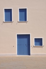 Closed blue windows and door on wall of mediterranean house during the siesta time