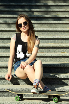 Beautiful tattooed girl with skateboard  on stairs, outdoors