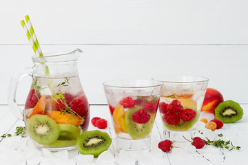Healthy detox fruit infused flavored water. Summer refreshing homemade cocktail with fruits and thyme on white wooden table