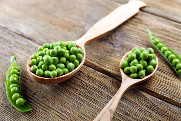 Fresh green peas in wooden spoon on table close up