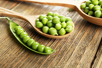 Fresh green peas in wooden spoon on table close up