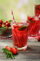 Full jug and glasses of strawberry juice with berries on bright background