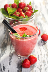 Glass of milkshake with strawberries on wooden table close up