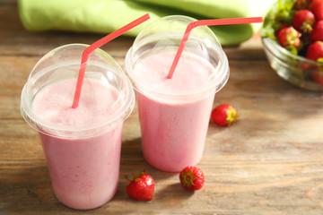 Plastic cups of milkshake with strawberries on table close up