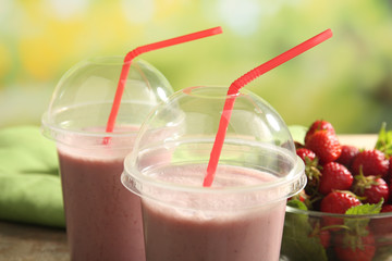 Glasses of milkshake with strawberries on bright background