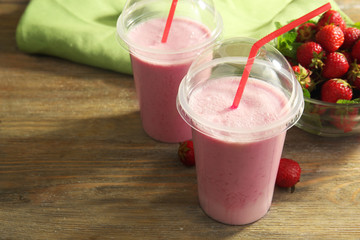 Plastic cups of milkshake with strawberries on table close up