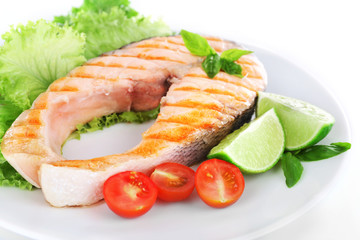 Tasty grilled salmon with tomato and lime on plate close up