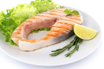 Tasty grilled salmon with lime and greens on plate close up