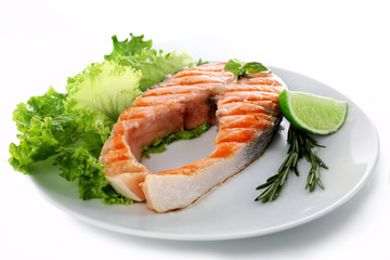 Tasty grilled salmon with lime and greens on plate close up