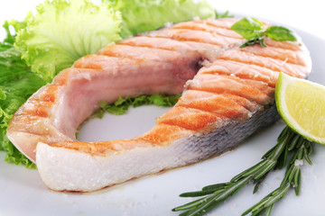 Tasty grilled salmon with lime and greens on plate close up