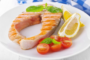 Tasty grilled salmon with tomato and lemon on table close up