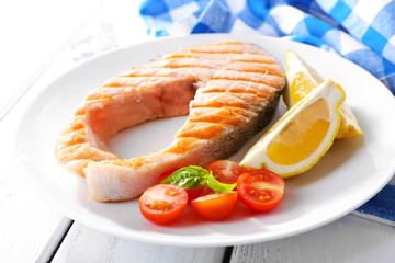 Tasty grilled salmon with tomato and lemon on table close up