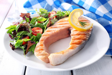 Tasty grilled salmon with salad on table close up