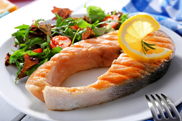 Tasty grilled salmon with salad on table close up
