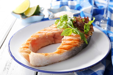 Tasty grilled salmon with greens on table close up